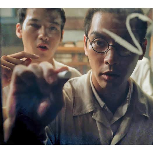 A man writing on a chalkboard with another man behind him watching.