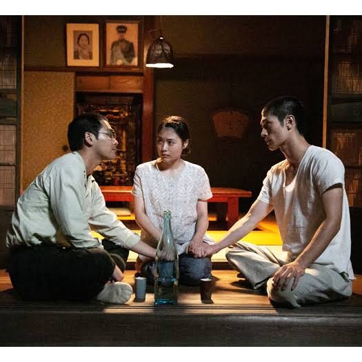 Two men and a woman sitting on the floor, holding hands.
