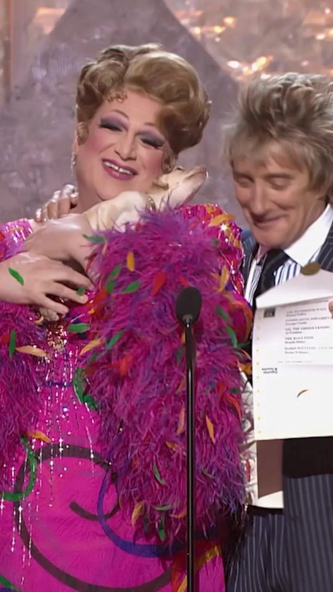 Harvey Fierstein in drag with a small dog next to Rod Stewart at the Grammies.