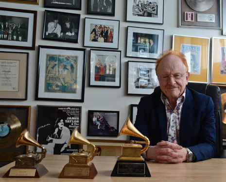 Peter Asher, three Grammies in front of him, wall of pictures and platinum album behind him.