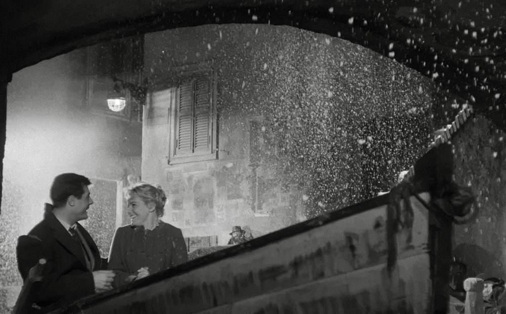 Schell and Mastroianni under a bridge smiling about snow falling.